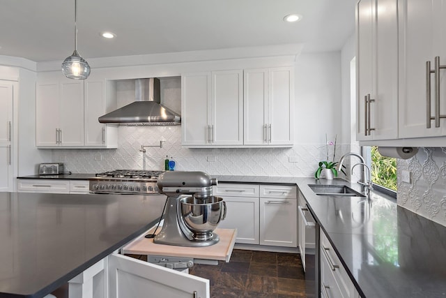 kitchen featuring dark countertops, stainless steel dishwasher, white cabinetry, a sink, and wall chimney exhaust hood