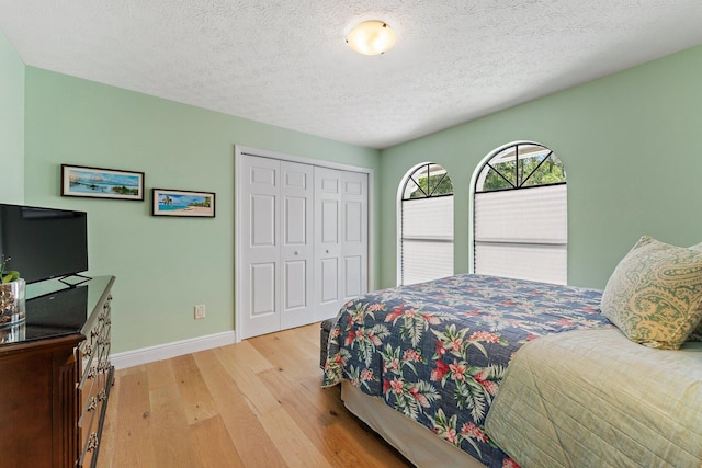bedroom with light wood-style flooring, a textured ceiling, baseboards, and a closet