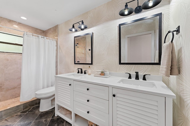 bathroom with a tile shower, double vanity, a sink, and toilet