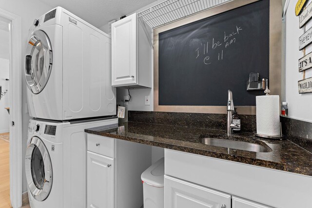 laundry room with light wood-type flooring, stacked washer and clothes dryer, cabinet space, and a sink