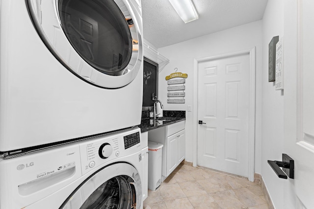 laundry room with cabinets, stacked washer and clothes dryer, sink, a textured ceiling, and light tile patterned flooring