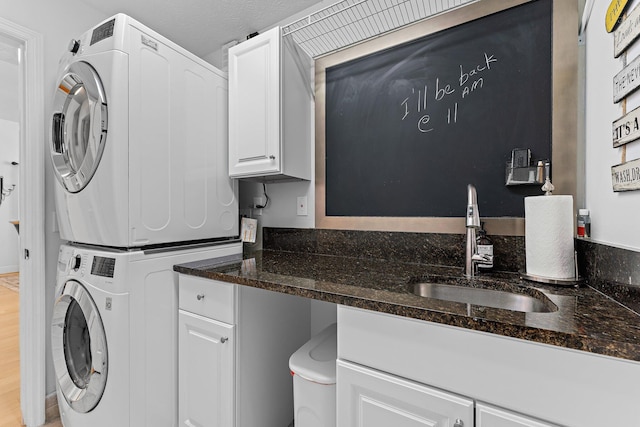 washroom featuring light hardwood / wood-style floors, stacked washer and dryer, cabinets, and sink