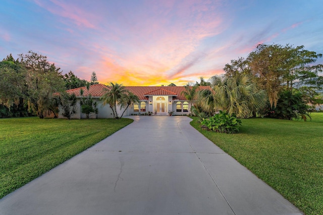 mediterranean / spanish house featuring driveway, a tile roof, a lawn, and stucco siding