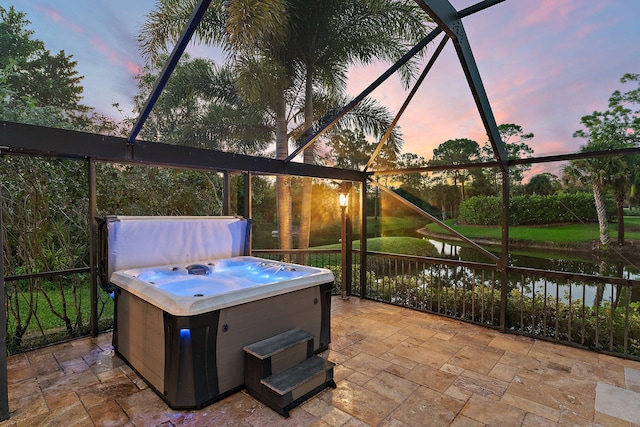 patio terrace at dusk with a water view, a hot tub, and a lanai