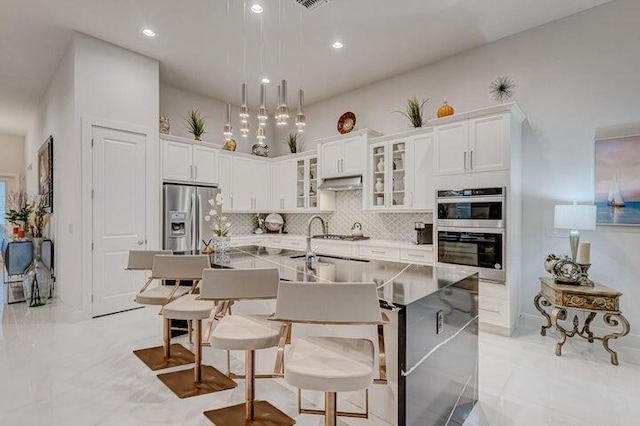 kitchen featuring light tile patterned floors, appliances with stainless steel finishes, white cabinets, a center island with sink, and tasteful backsplash