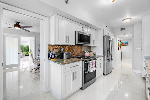 kitchen with dark stone counters, ceiling fan, light tile patterned floors, stainless steel appliances, and white cabinets