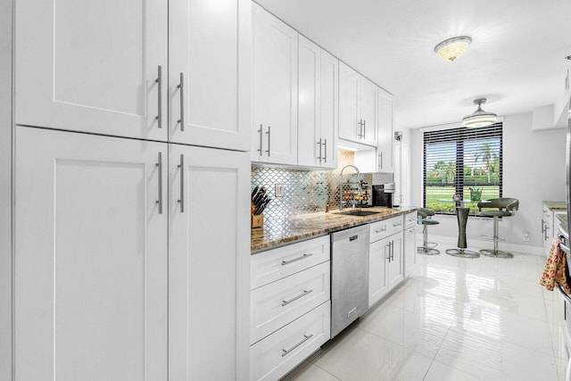 kitchen with sink, light tile patterned floors, dishwashing machine, stone countertops, and white cabinetry