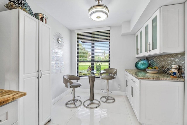 kitchen with light stone counters, white cabinetry, light tile patterned floors, and tasteful backsplash