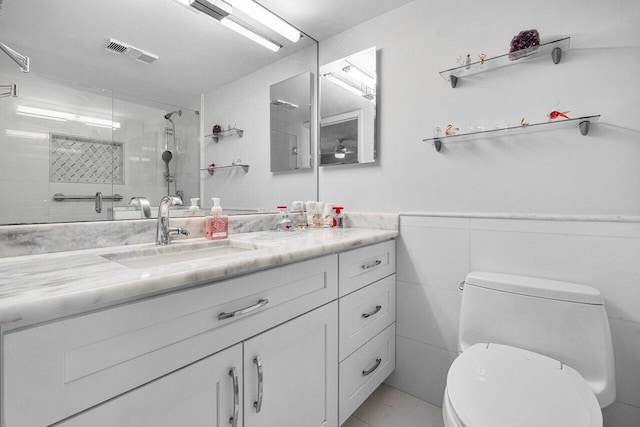 bathroom featuring vanity, tile patterned floors, tiled shower, tile walls, and toilet