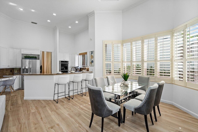 dining space featuring ornamental molding, light hardwood / wood-style floors, and a towering ceiling