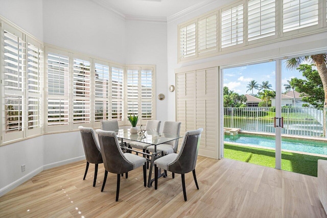 dining area with ornamental molding, light hardwood / wood-style flooring, a water view, and a high ceiling