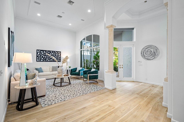 living room with french doors, decorative columns, crown molding, light wood-type flooring, and a high ceiling