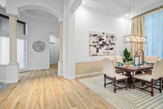 dining room featuring ornamental molding, a towering ceiling, wood-type flooring, and decorative columns