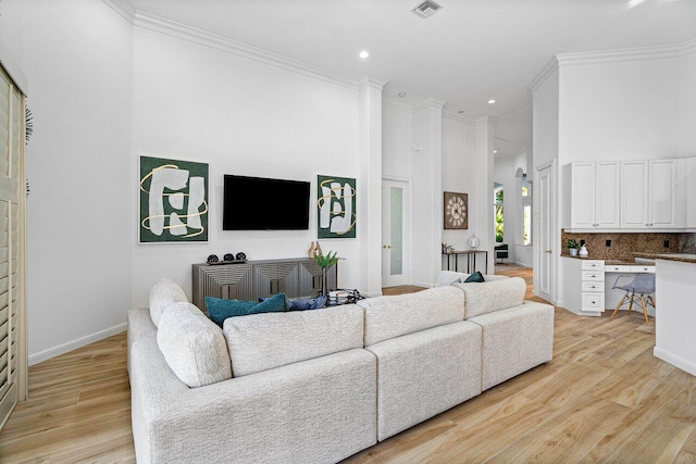 living room featuring ornamental molding, built in desk, light hardwood / wood-style floors, and a towering ceiling