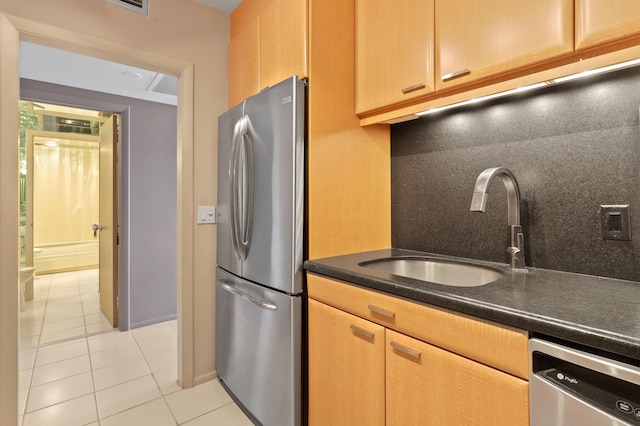 kitchen with tasteful backsplash, dark countertops, appliances with stainless steel finishes, a sink, and light tile patterned flooring