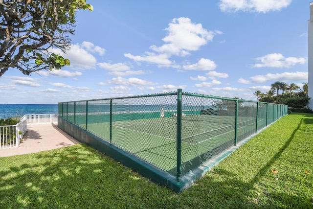 view of tennis court featuring a water view and a lawn