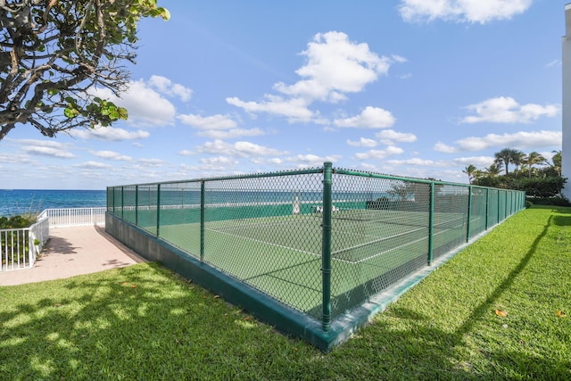 view of sport court featuring a yard, a water view, and fence