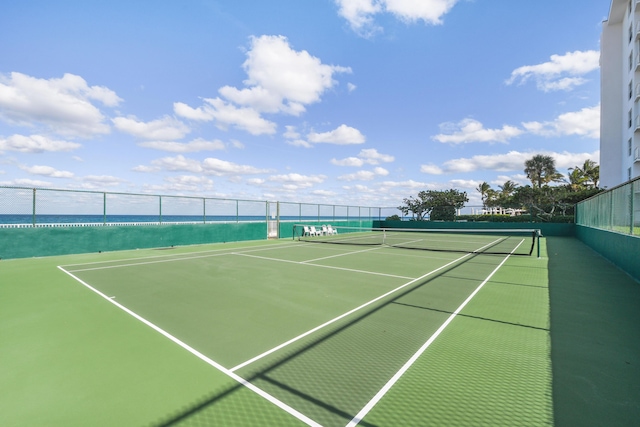 view of tennis court featuring a water view and fence