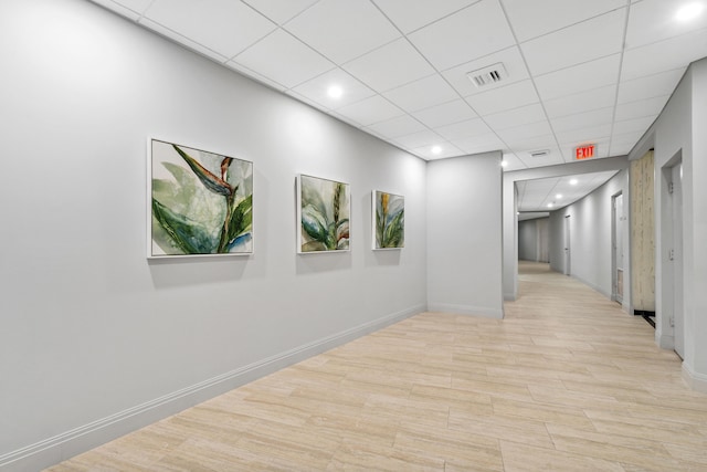 hall with light wood-style flooring, a paneled ceiling, visible vents, and baseboards