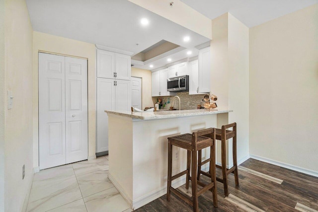 kitchen featuring white cabinetry, light stone countertops, light hardwood / wood-style floors, kitchen peninsula, and backsplash