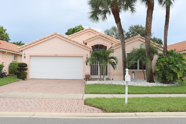 mediterranean / spanish home with decorative driveway, a tile roof, an attached garage, and stucco siding