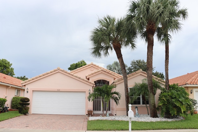 mediterranean / spanish-style house with a garage, a tile roof, decorative driveway, and stucco siding