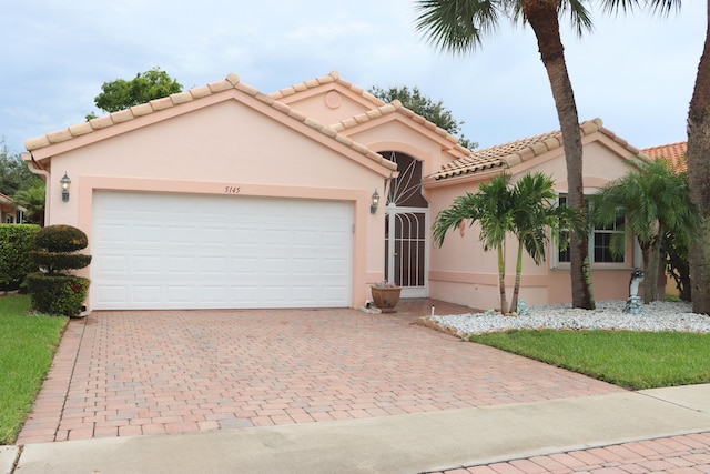 mediterranean / spanish-style home with a tiled roof, decorative driveway, an attached garage, and stucco siding