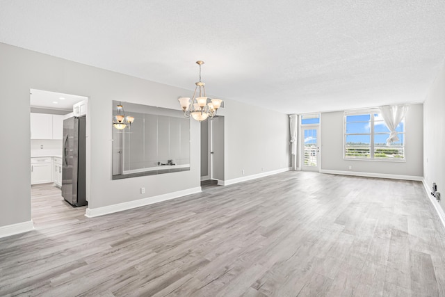 unfurnished living room featuring a chandelier, a textured ceiling, and light wood-type flooring