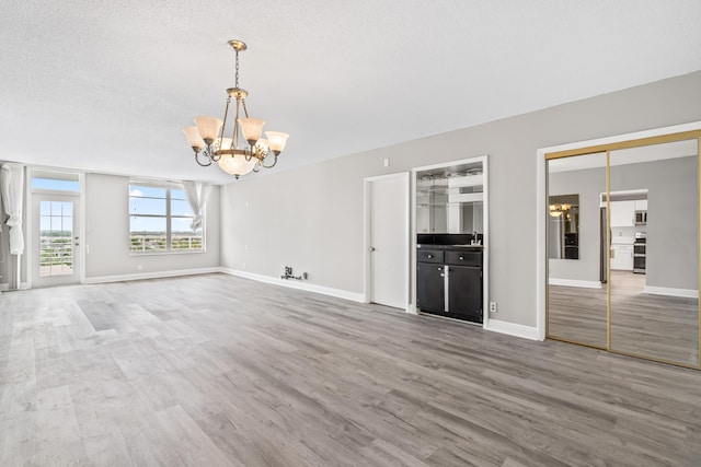 unfurnished living room featuring sink, hardwood / wood-style floors, a textured ceiling, and a notable chandelier