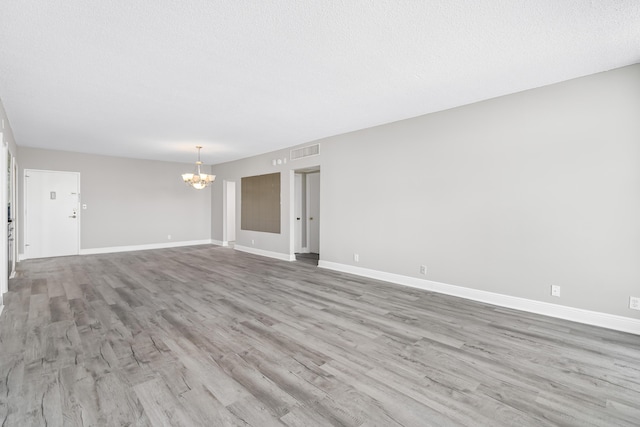 unfurnished room with a chandelier, light hardwood / wood-style floors, and a textured ceiling