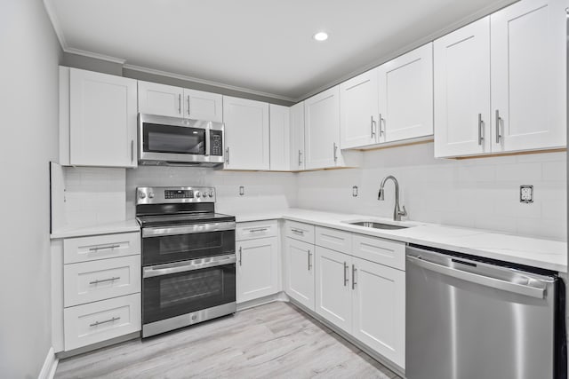 kitchen with sink, appliances with stainless steel finishes, white cabinetry, tasteful backsplash, and light hardwood / wood-style floors