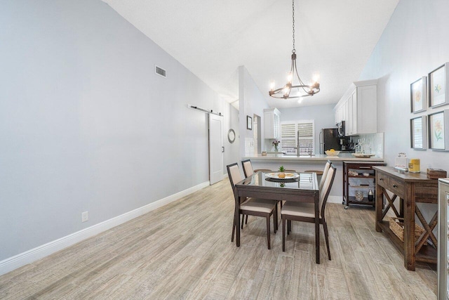 dining room featuring a notable chandelier, a barn door, light wood-type flooring, and high vaulted ceiling