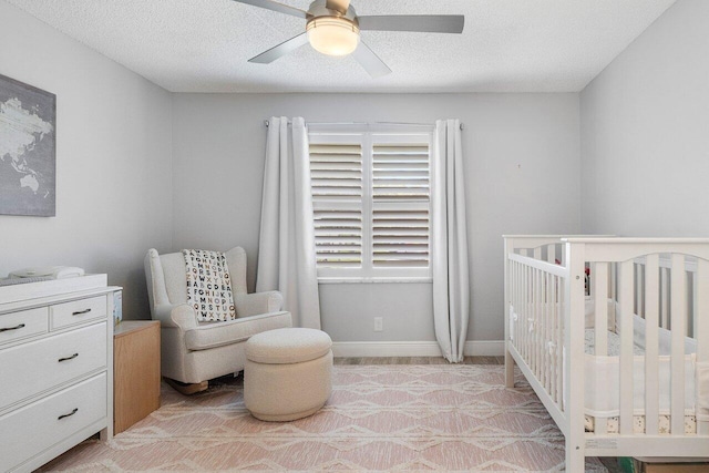 bedroom featuring a textured ceiling, a nursery area, and ceiling fan