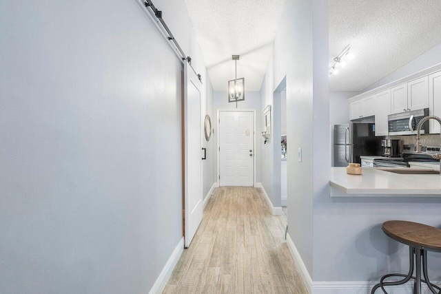 kitchen with white cabinetry, light wood-type flooring, a textured ceiling, a barn door, and stainless steel appliances