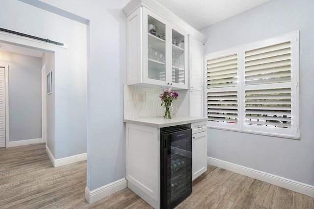 bar featuring a barn door, white cabinetry, beverage cooler, and light hardwood / wood-style floors