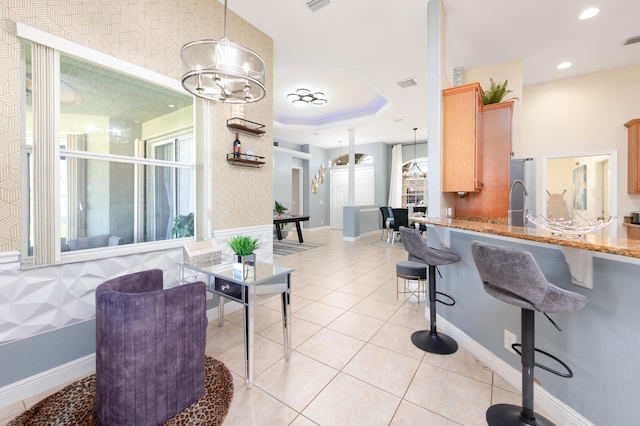 kitchen featuring decorative light fixtures, a kitchen bar, light stone counters, a raised ceiling, and light tile patterned floors