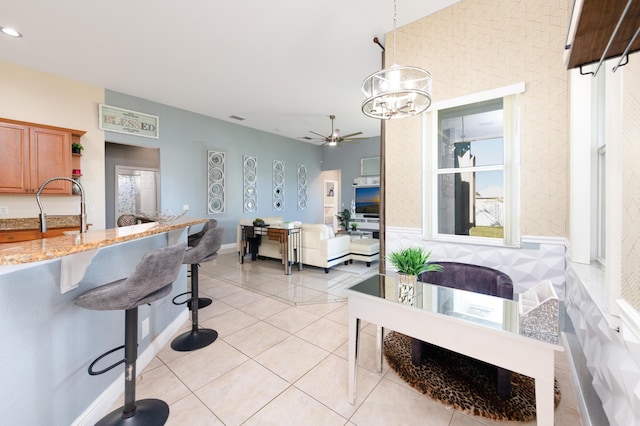 kitchen featuring pendant lighting, a kitchen bar, light tile patterned floors, light stone counters, and a sink