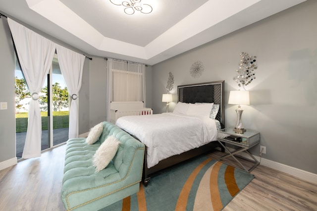 bedroom with access to exterior, hardwood / wood-style floors, and a tray ceiling