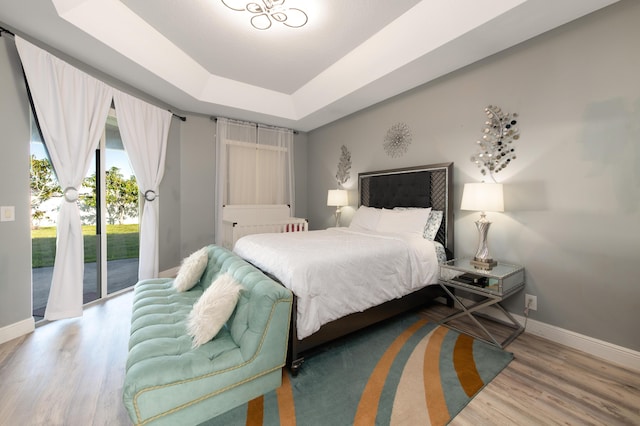 bedroom with a tray ceiling, baseboards, wood finished floors, and access to outside