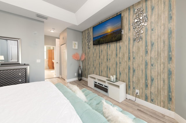 bedroom featuring visible vents, ensuite bath, baseboards, and wood finished floors