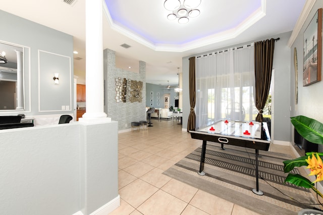 recreation room featuring decorative columns, light tile patterned floors, a raised ceiling, and crown molding