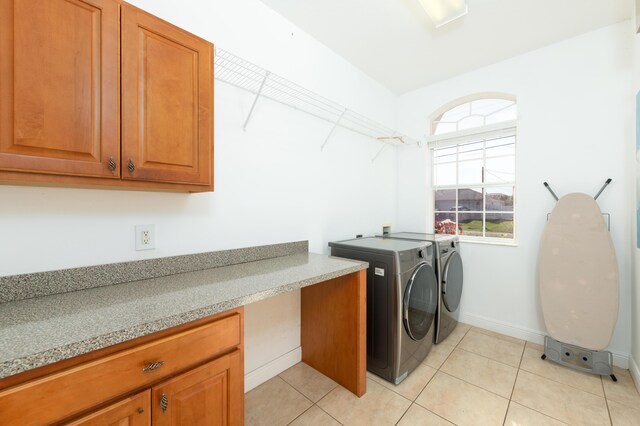 clothes washing area with cabinets, washing machine and dryer, and light tile patterned floors