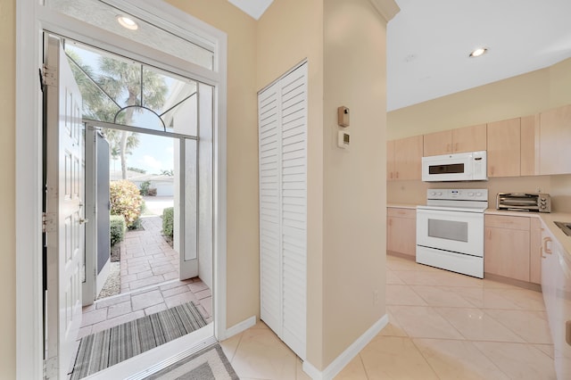 kitchen with light tile patterned floors, white appliances, and light brown cabinetry