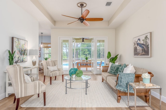 living room with light hardwood / wood-style floors, ceiling fan, and a tray ceiling