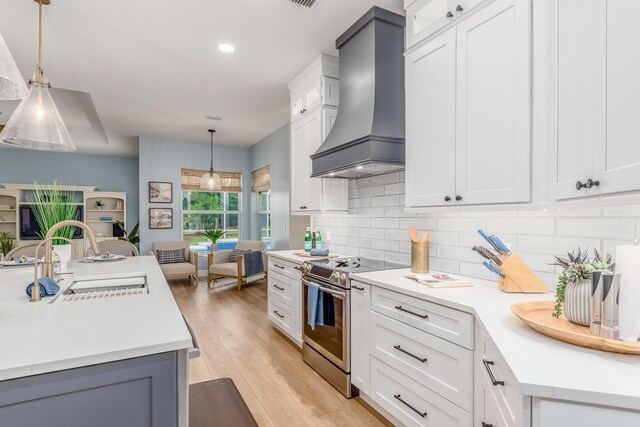 kitchen featuring white cabinets, electric stove, premium range hood, pendant lighting, and a sink