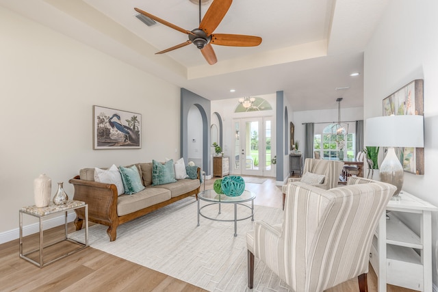 living room featuring ceiling fan with notable chandelier, a raised ceiling, and light wood-type flooring