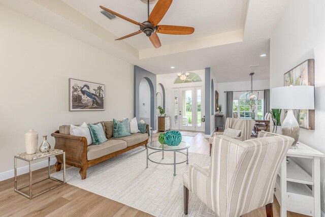 living area featuring light wood-style floors, a raised ceiling, visible vents, and baseboards