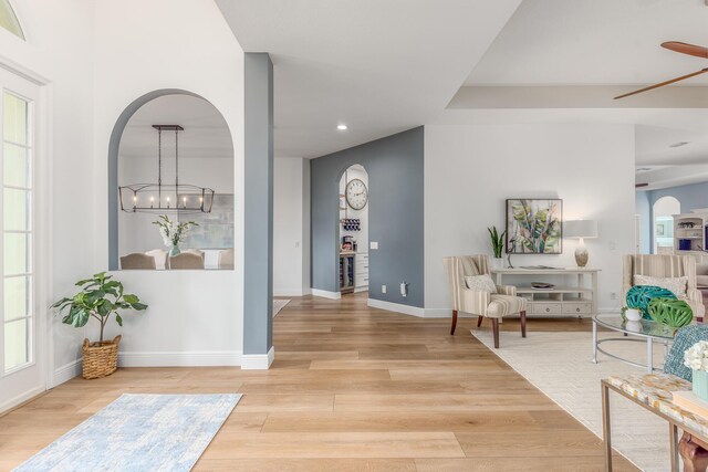 sitting room featuring arched walkways, recessed lighting, light wood-style floors, baseboards, and ceiling fan with notable chandelier