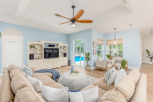 living room with light hardwood / wood-style floors, ceiling fan, and a tray ceiling