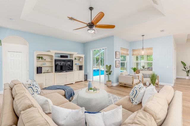 living area with ceiling fan, arched walkways, baseboards, light wood-type flooring, and a raised ceiling